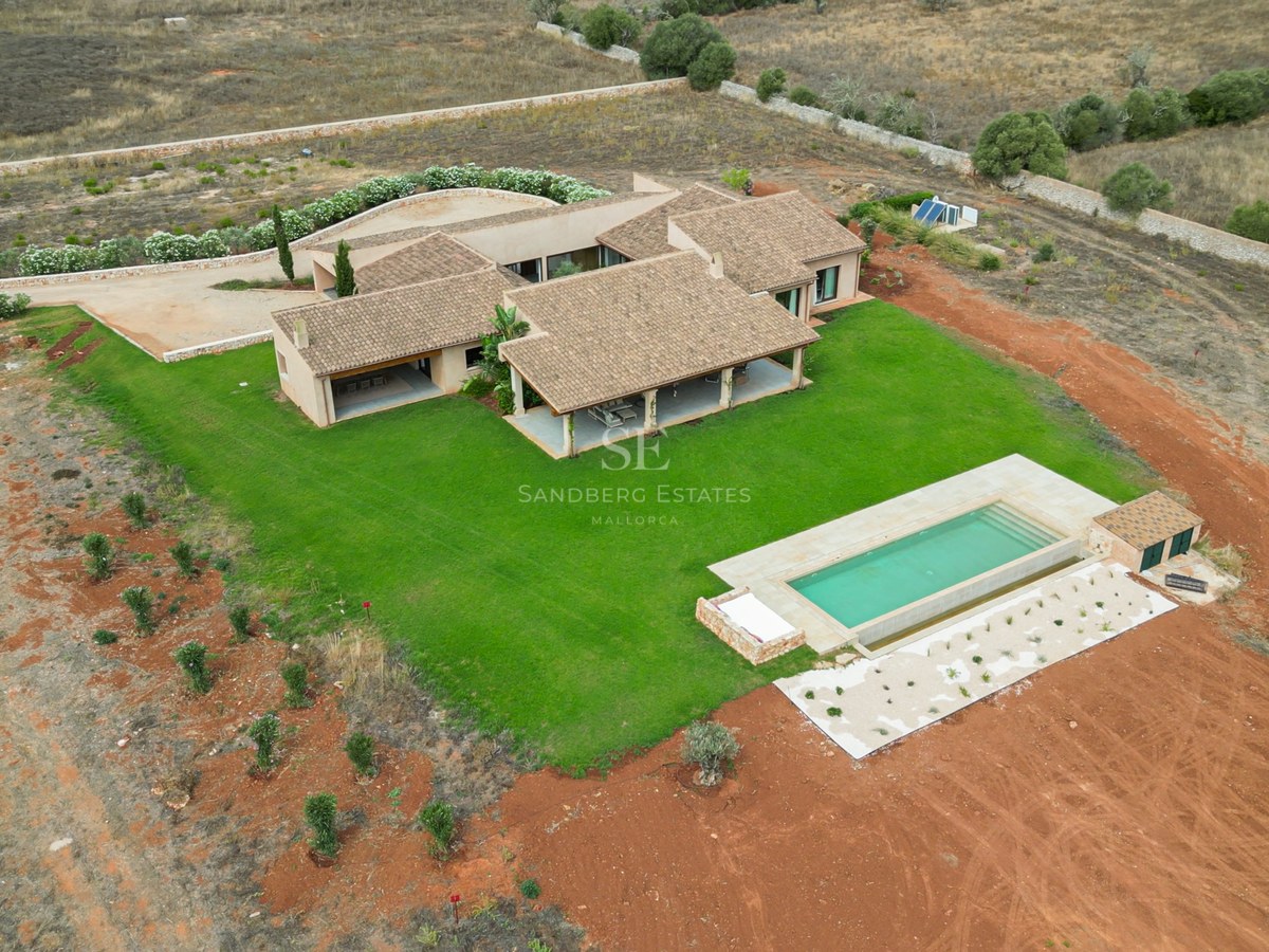 Aerial drone shot of a modern villa with terracotta roof, green lawn, and rectangular pool in the countryside.