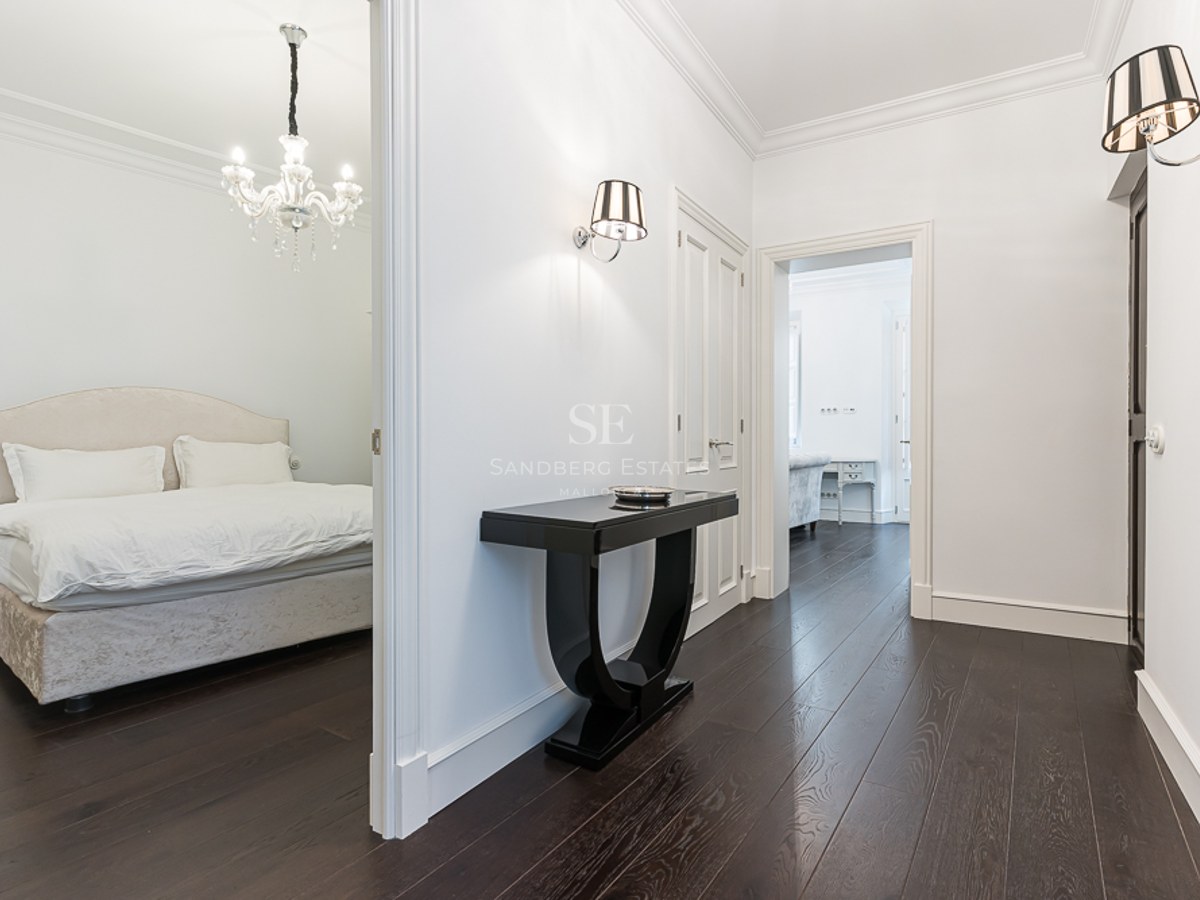 Bright hallway with dark wood floors, black console table, and view into a bedroom with a crystal chandelier.