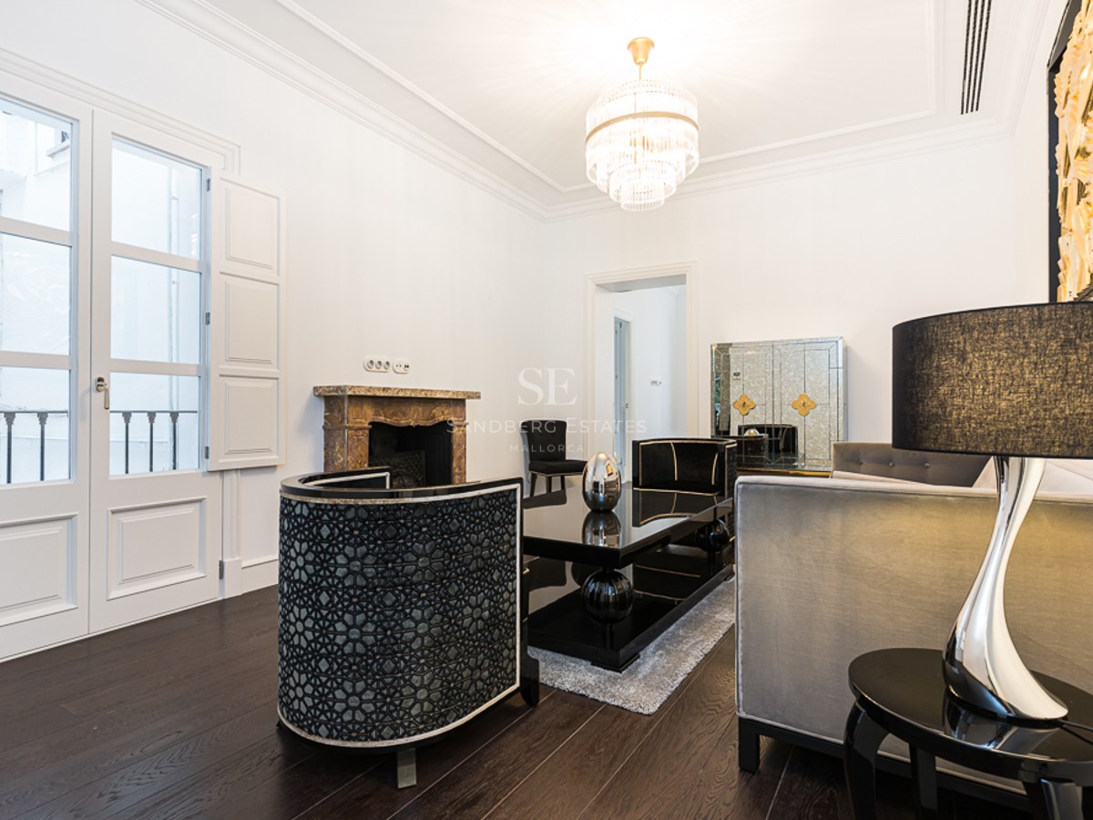 Elegant living room with white walls, dark wood floors, designer furniture, crystal chandelier, and a marble fireplace.