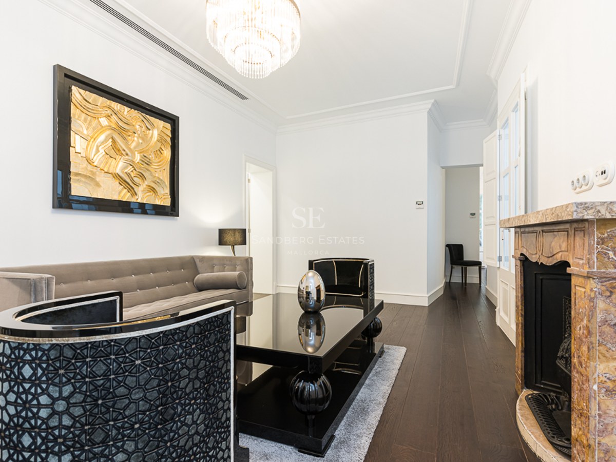 Luxury living room with grey velvet sofa, black table, marble fireplace, and gold wall art.