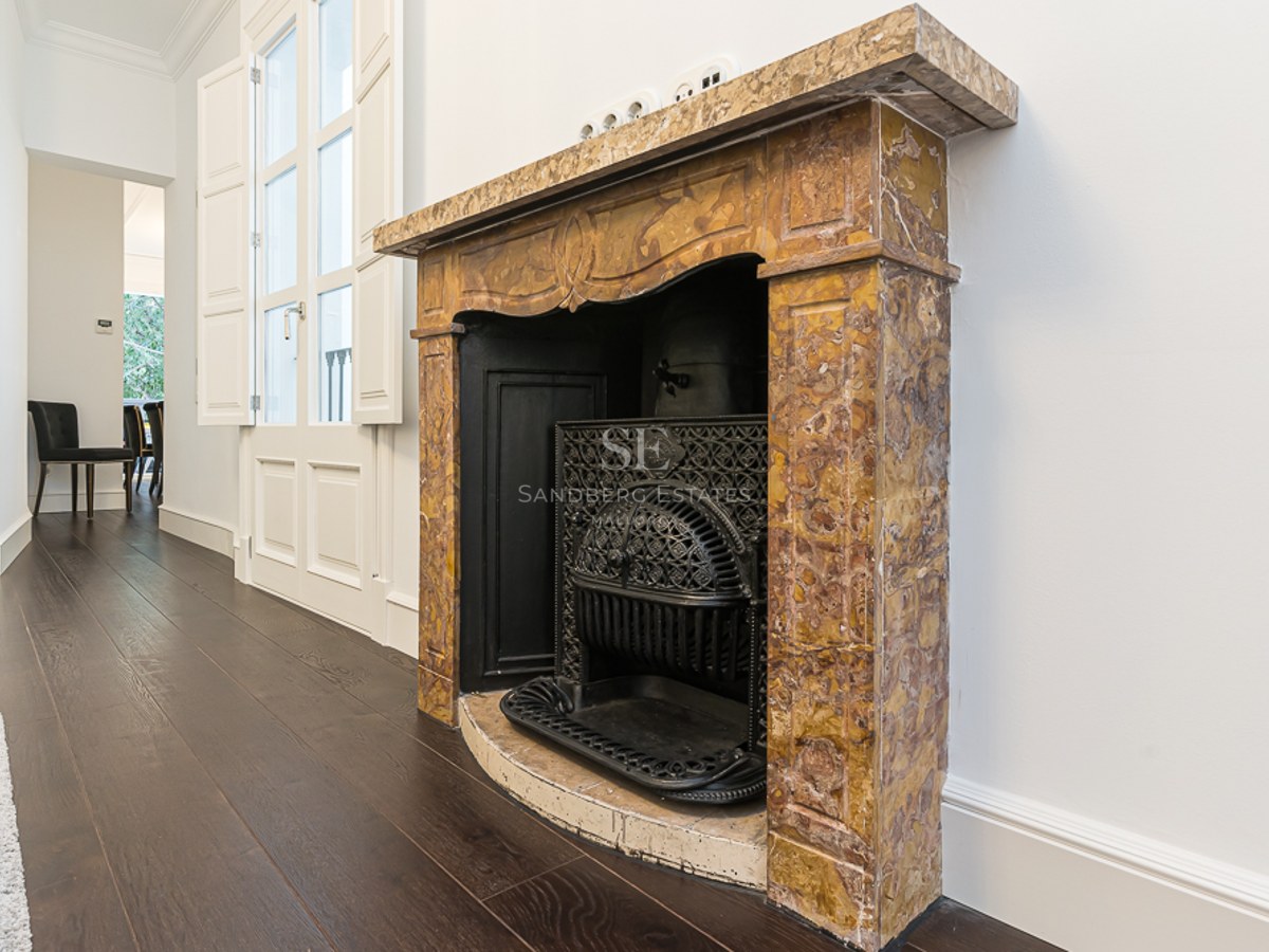 Ornate yellow marble fireplace with a decorative black cast iron grate on dark wood flooring against white walls.