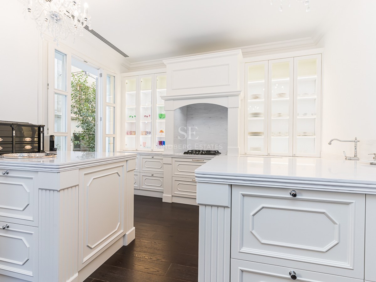 Elegant kitchen featuring white cabinetry, marble countertops, a central island, and a crystal chandelier.