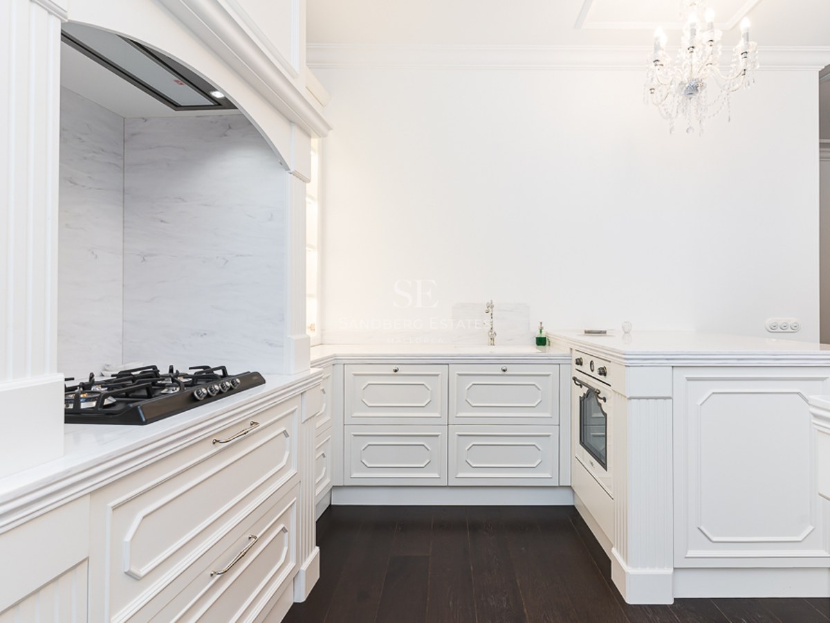Elegant white kitchen with marble countertops, dark wood flooring, and a crystal chandelier.