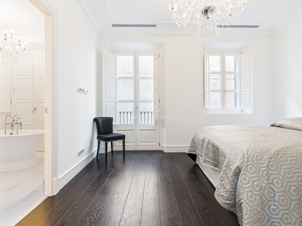 Master bedroom featuring dark wood floors, crystal chandelier, and a view into a marble bathroom with a bathtub.