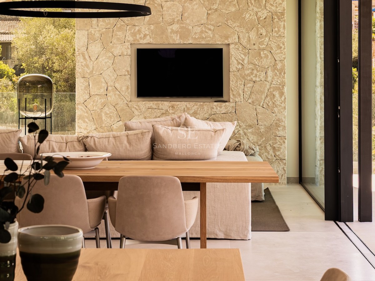 Modern living room with a stone feature wall, recessed TV, plush beige sofa, and a wooden dining table in the foreground.