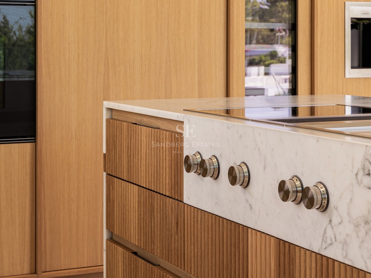 Close-up of a white marble kitchen island featuring brushed metal control knobs and fluted light wood cabinetry.