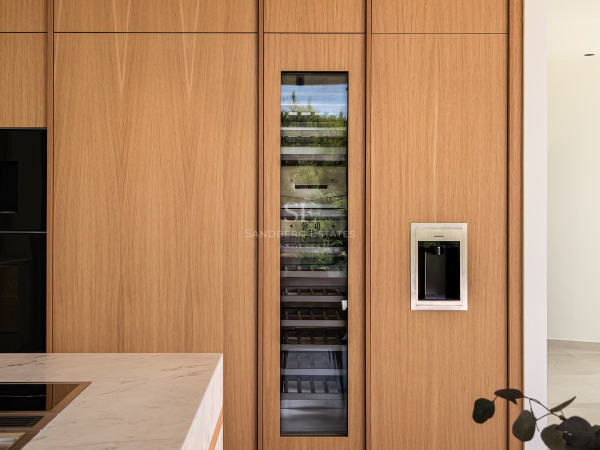 A luxury kitchen with floor-to-ceiling oak cabinetry, an integrated glass-door wine cooler, and a marble island.