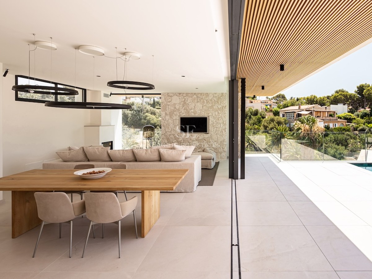A luxury open-plan living and dining room with glass walls opening onto a terrace and infinity pool.