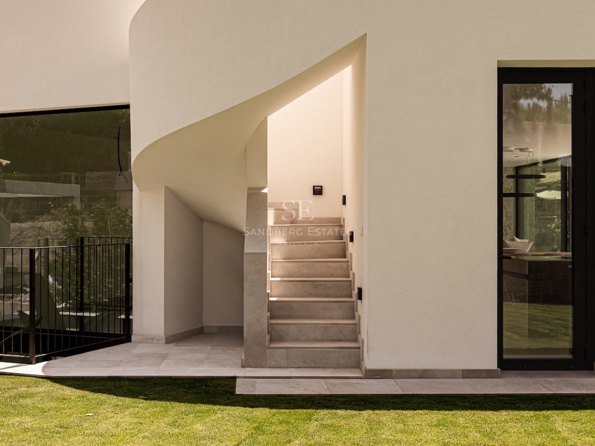 Exterior view of a modern white building featuring a stone staircase, a curved wall, and large black-framed windows.