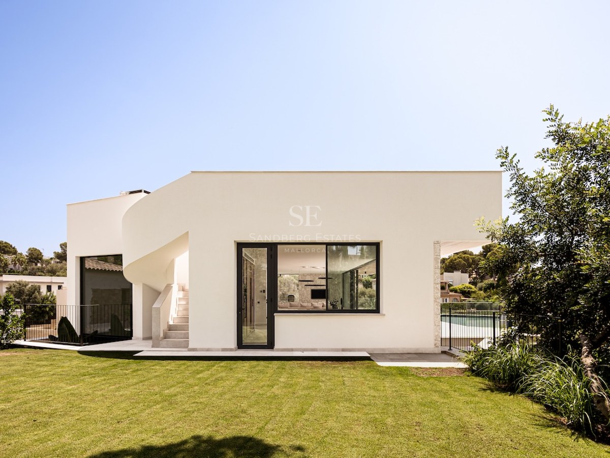 Villa blanche moderne avec escalier extérieur courbé et pelouse verdoyante sous un ciel bleu.