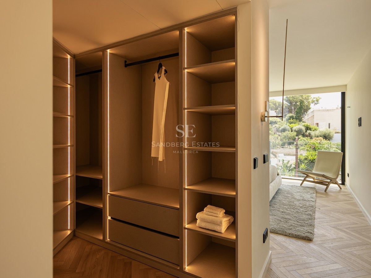 A modern walk-in closet with light wood shelving, integrated vertical LED strips, and herringbone parquet flooring.