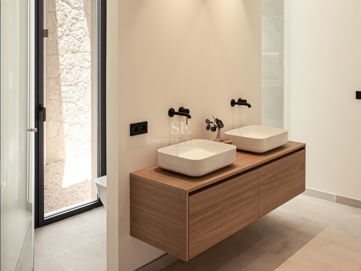 Salle de bain minimaliste avec double vasque sur meuble en bois, robinetterie noire et patio extérieur en pierre.