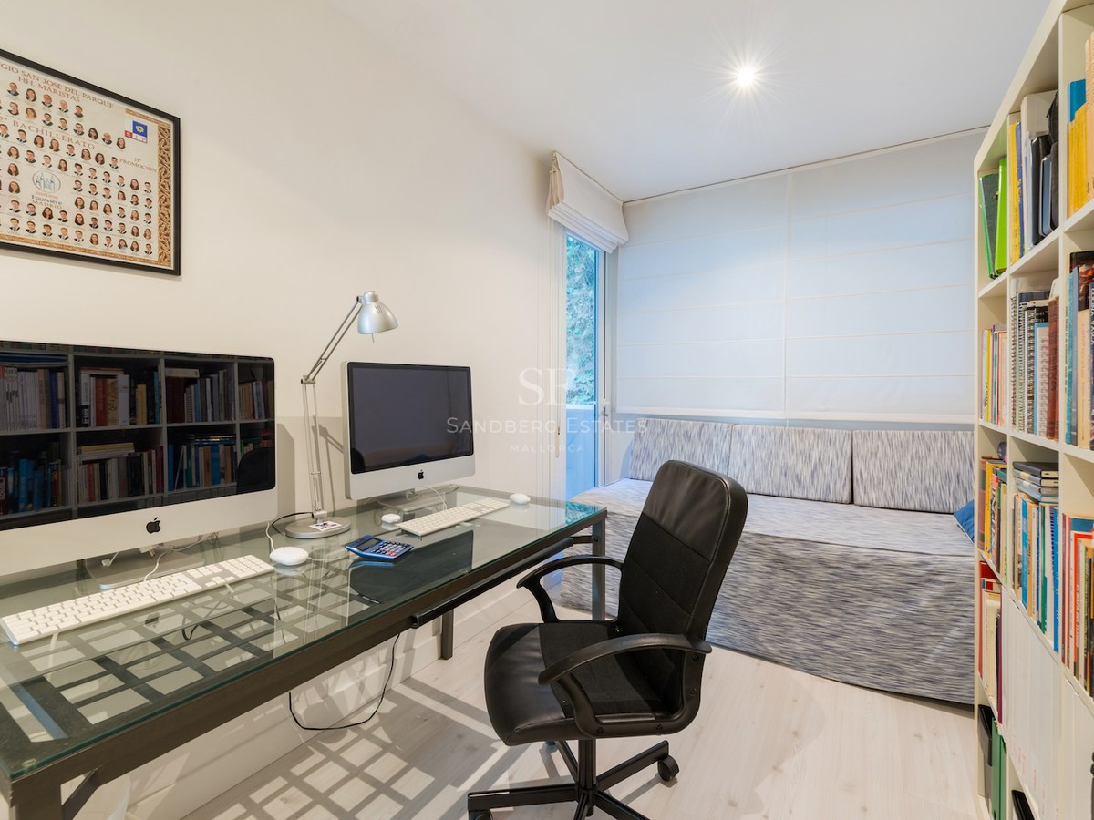 Un bureau lumineux avec un bureau en verre, deux ordinateurs, une chaise ergonomique noire et de grandes étagères.