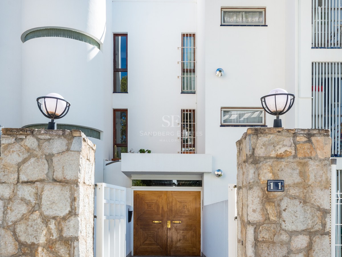 High-contrast view of a white villa entrance featuring natural stone pillars and solid wooden doors in bright daylight.