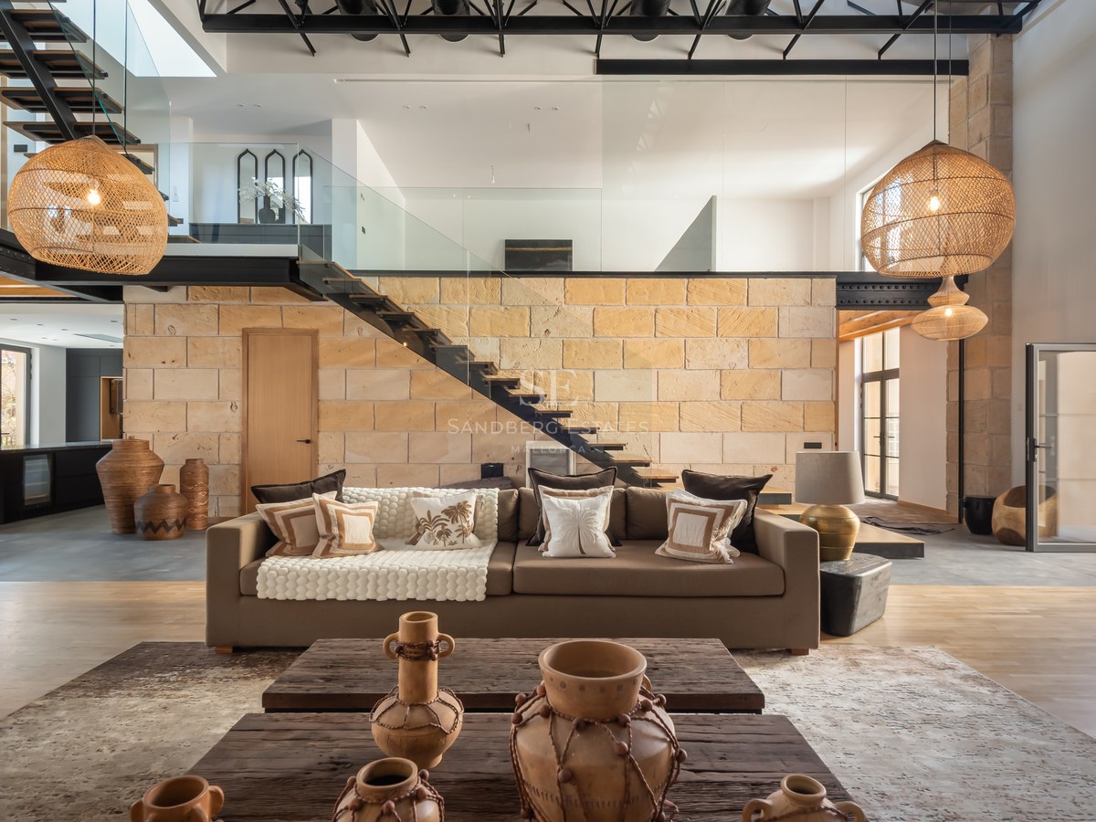 Modern living room featuring a stone wall, floating staircase, large wicker lamps, and a comfortable brown sofa.
