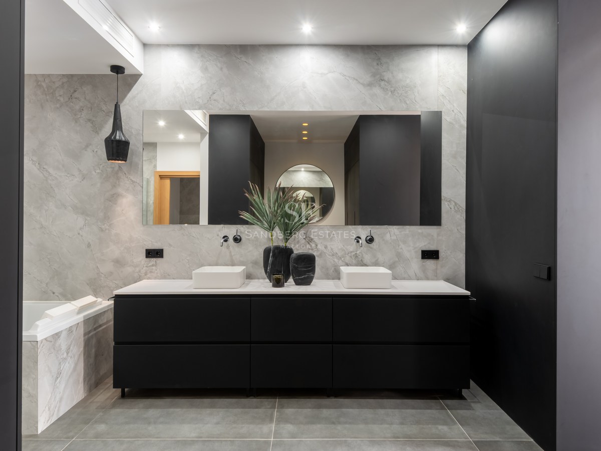 Luxury bathroom with marble walls, double white basins on a black vanity unit, and a large mirror.