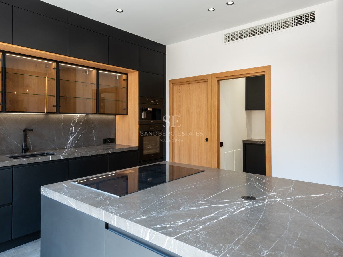 Modern kitchen featuring matte black cabinets, grey marble countertops, and warm wood accents.