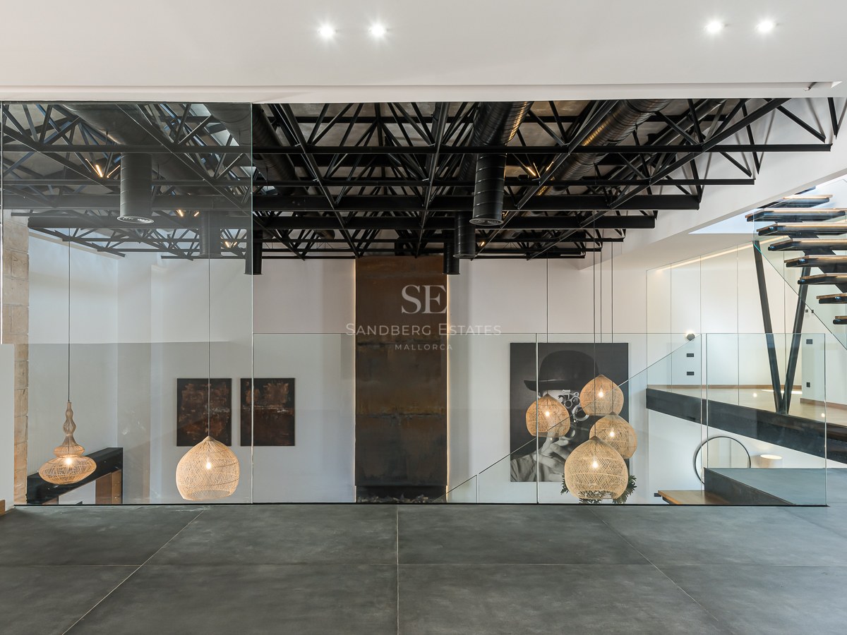 Modern interior featuring black steel ceiling trusses, glass railings, floating wood stairs, and designer pendant lamps.