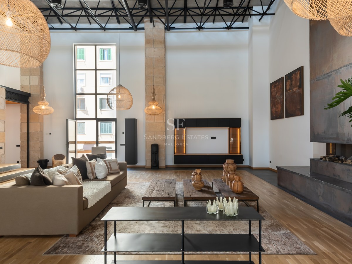 Modern living room with double-height ceilings, beige sofas, metal fireplace, and large wicker pendant lights.