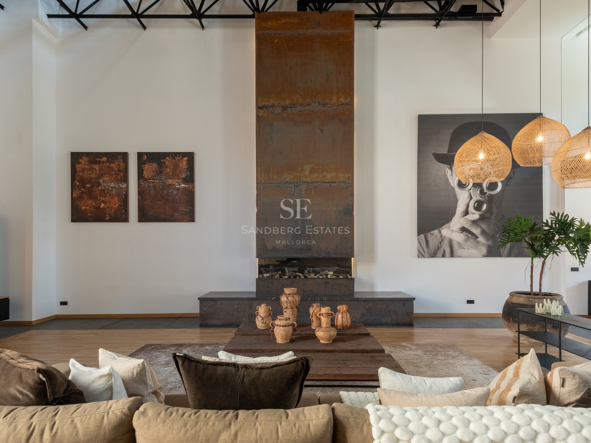 Spacious living room with a tall weathered steel fireplace, beige sofa, and woven pendant lamps in an industrial loft.