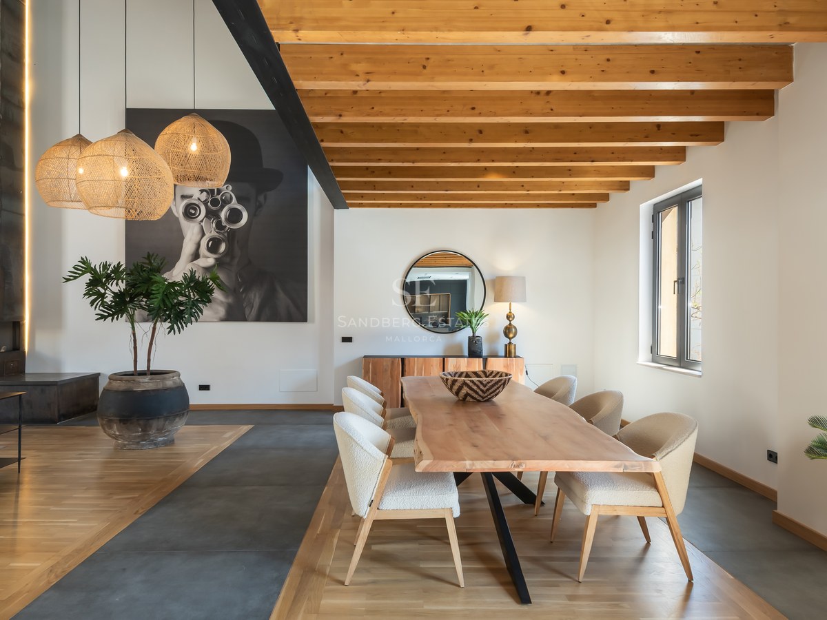 Elegant dining room featuring a live-edge wooden table, upholstered chairs, exposed ceiling beams, and large wall art.