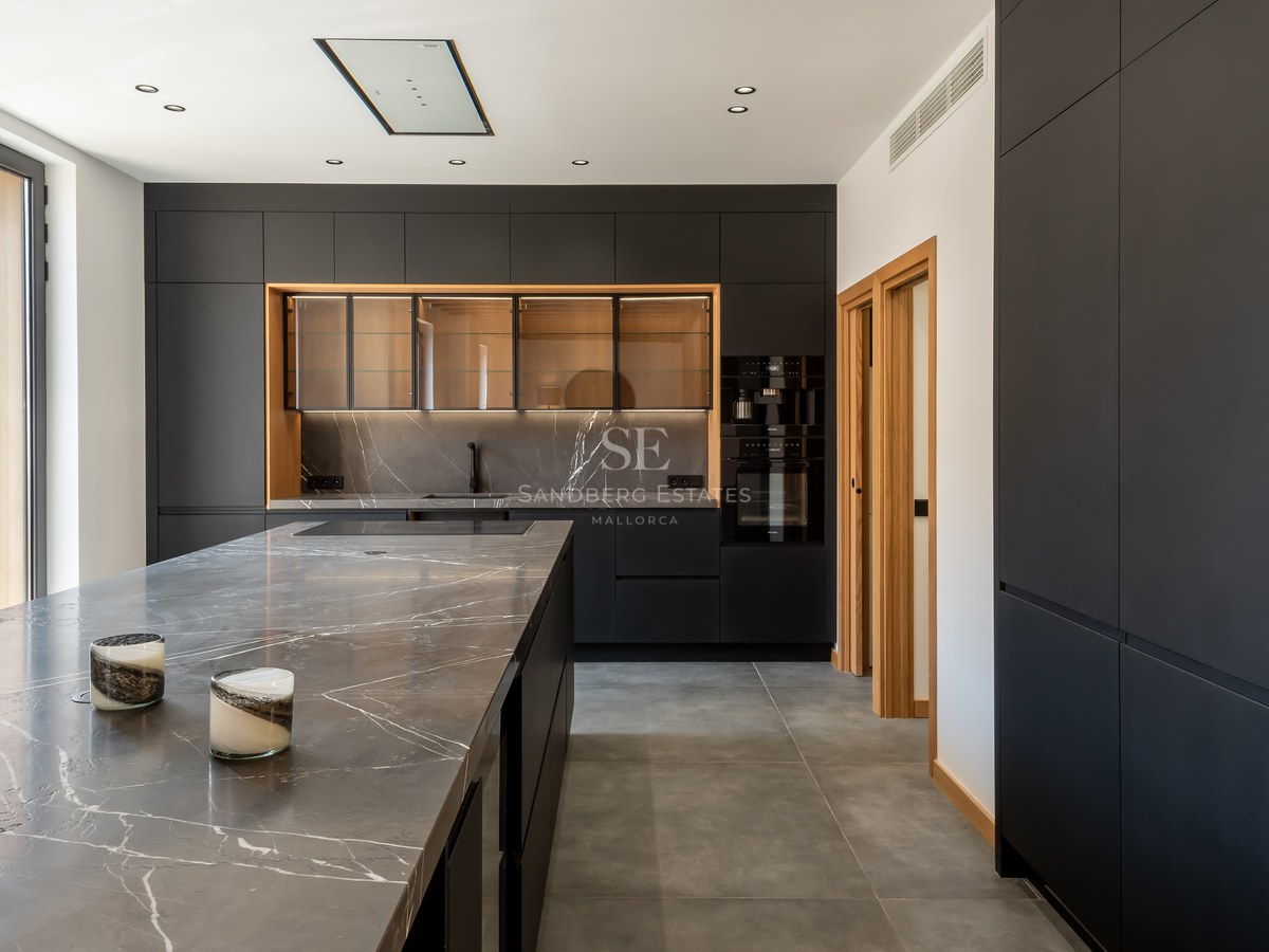 Modern kitchen featuring matte black cabinetry, grey veined marble countertops, and large windows.