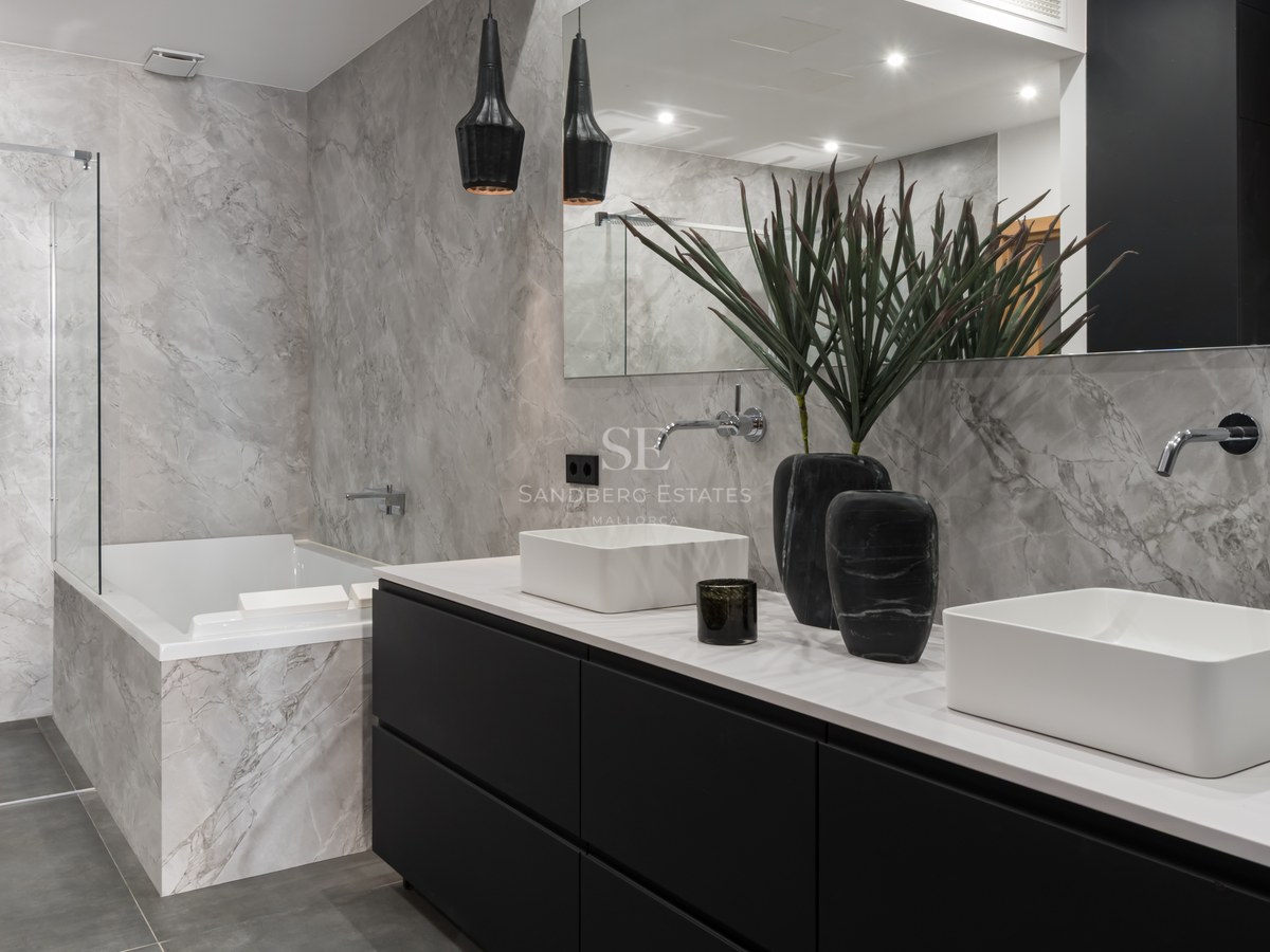 Luxury bathroom with double white sinks, black vanity, marble-tiled bathtub, and a glass-enclosed walk-in shower.