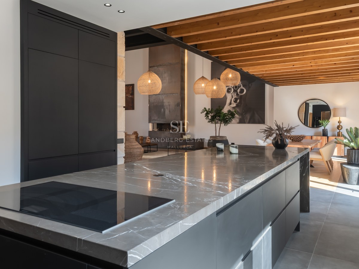 Modern kitchen featuring a large grey marble island, matte black cabinets, and exposed wooden ceiling beams.