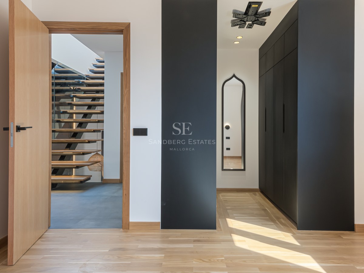 Modern hallway with light wood floors, black built-in closets, and an open door viewing a floating wooden staircase.