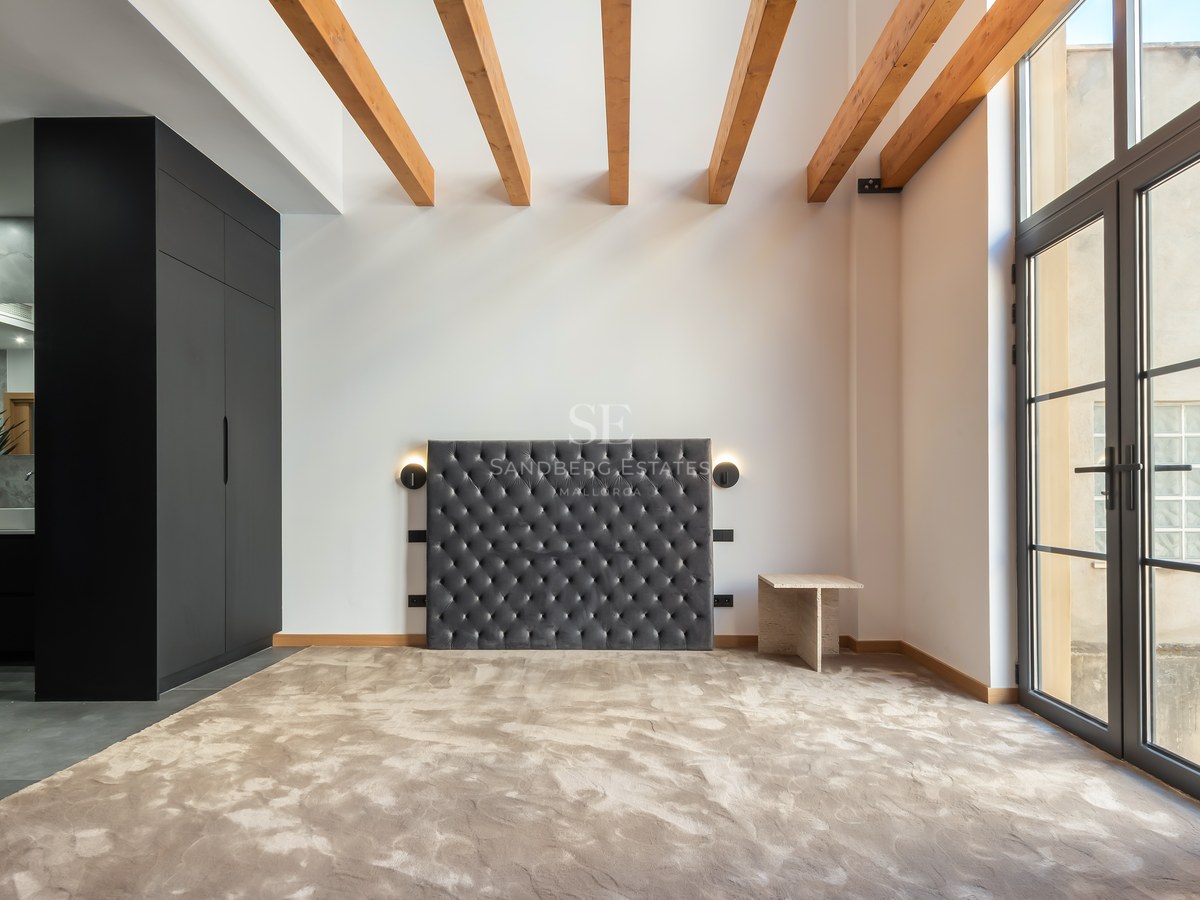 Bedroom featuring a grey velvet tufted headboard, wooden ceiling beams, black wardrobe, and large glass doors.