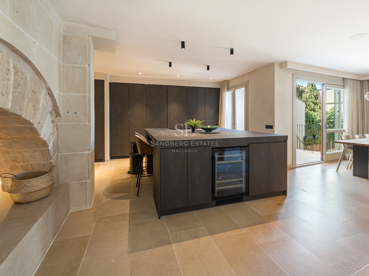 Modern kitchen with dark island and wine fridge next to a rustic stone arch and open-plan dining area.