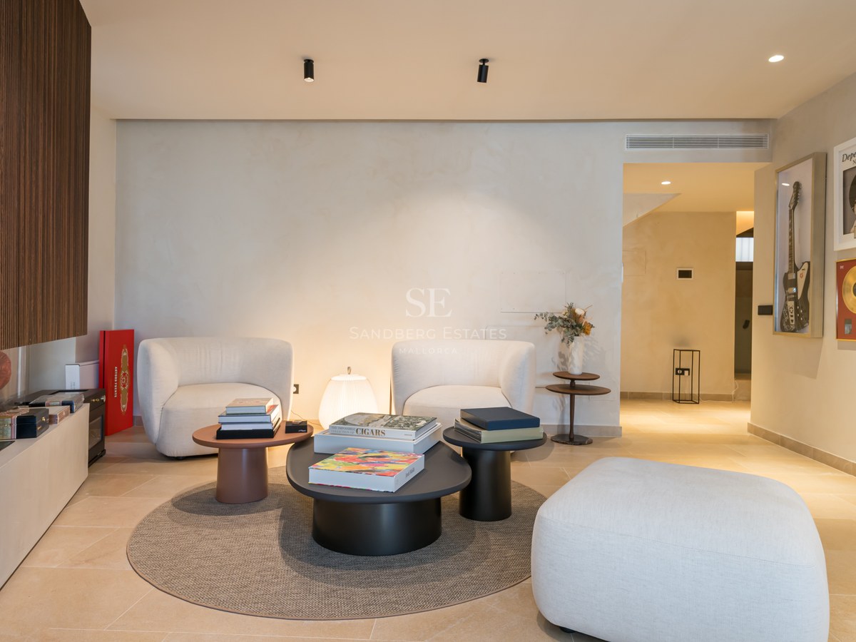 Modern living space with two white armchairs, coffee tables, a wood-slatted fireplace, and music-themed wall art.