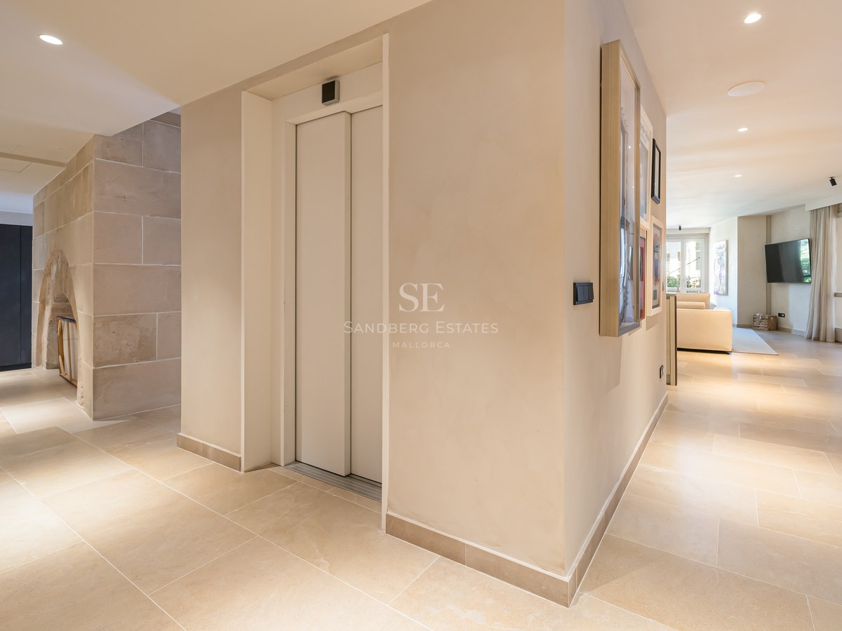 Spacious modern home entrance featuring a private elevator, beige stone floors, and a view into a bright living room.