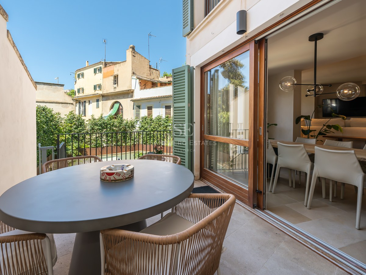 Sunny terrace with a gray oval dining table and wicker chairs next to large sliding glass doors.
