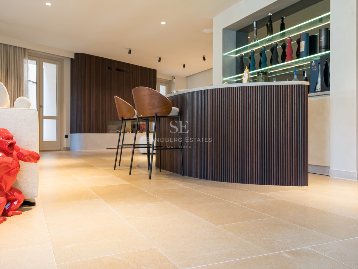 Modern living room featuring a curved wooden bar, designer stools, stone floors, and a bright red gorilla sculpture.