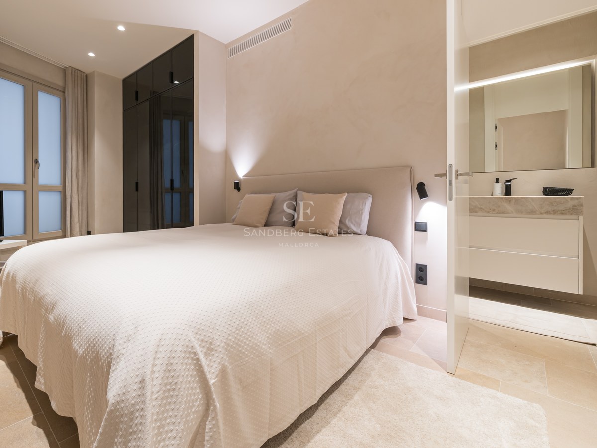 A contemporary bedroom featuring a large bed, dark glass wardrobes, and an open door leading to a modern bathroom.