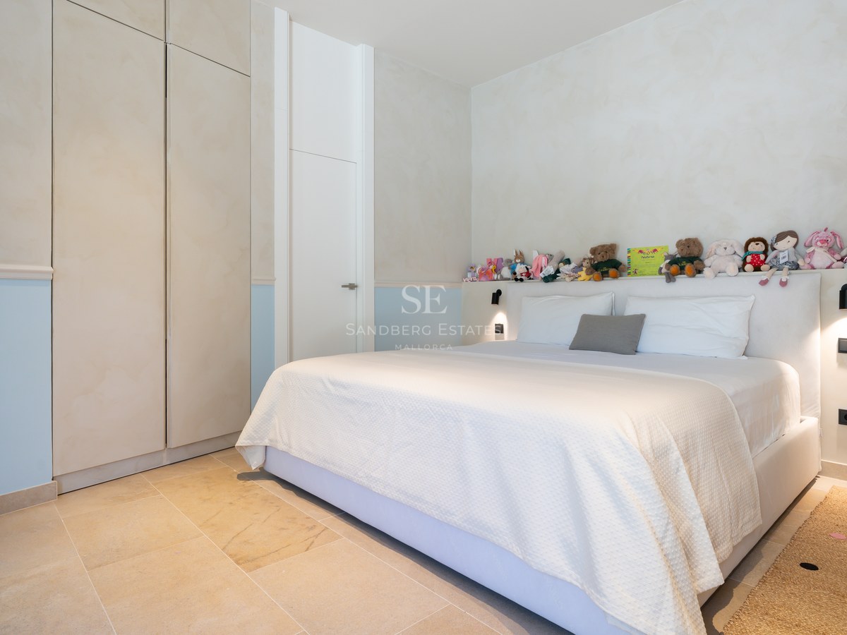 Bright bedroom featuring a large bed, stone floors, built-in wardrobes, and a row of stuffed animals on the headboard shelf.