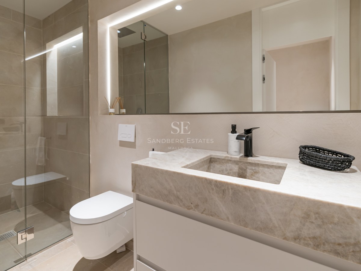 Modern bathroom featuring a stone vanity with integrated sink, black faucet, backlit mirror, and glass walk-in shower.