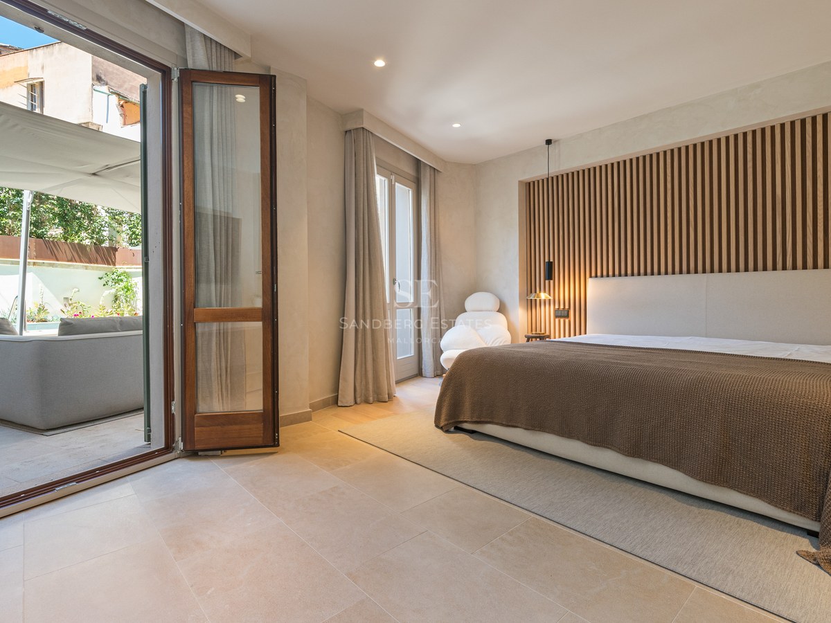 Modern master bedroom with wooden slat wall and large glass doors opening to a sunny private terrace.