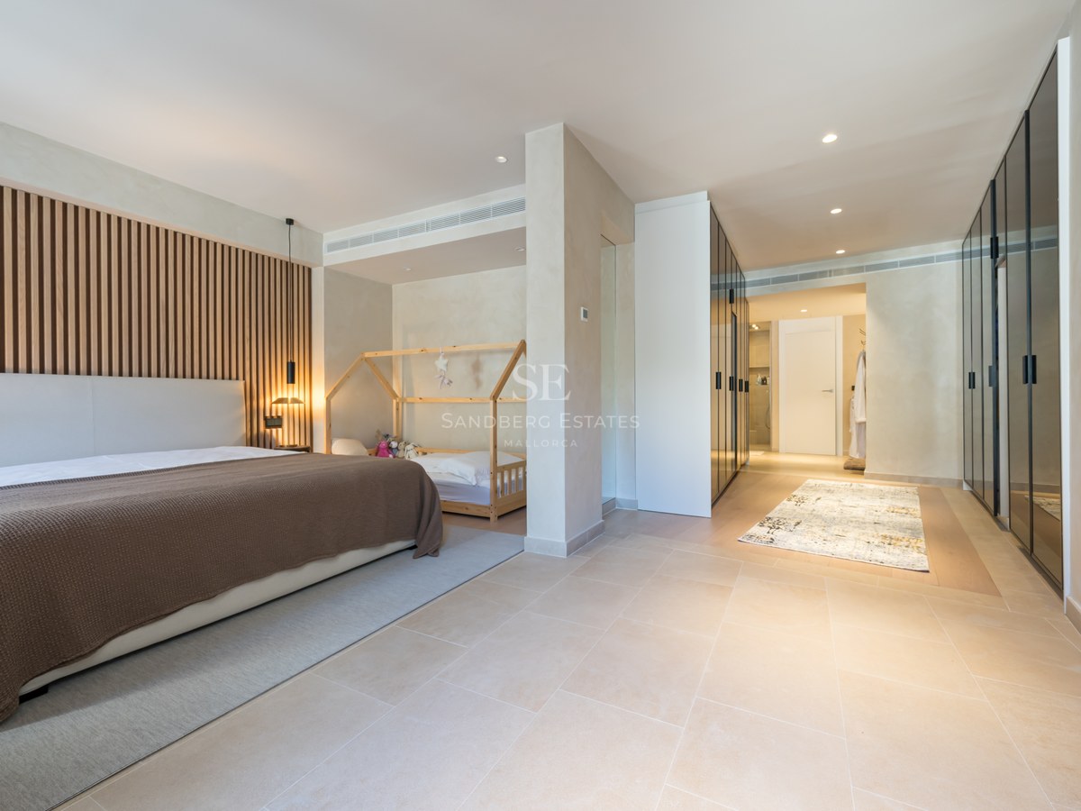 Modern bedroom featuring a wood slat wall, large bed, toddler area, and sleek glass-fronted wardrobes.