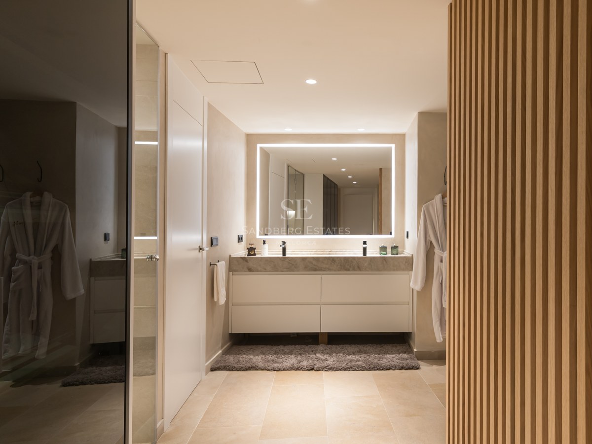 Modern bathroom featuring a marble double vanity, large backlit LED mirror, and vertical wood slat wall.