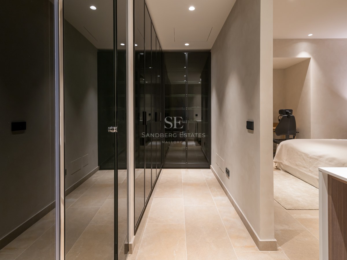 Minimalist master bedroom featuring sleek dark glass wardrobes, stone tile flooring, and warm recessed lighting.