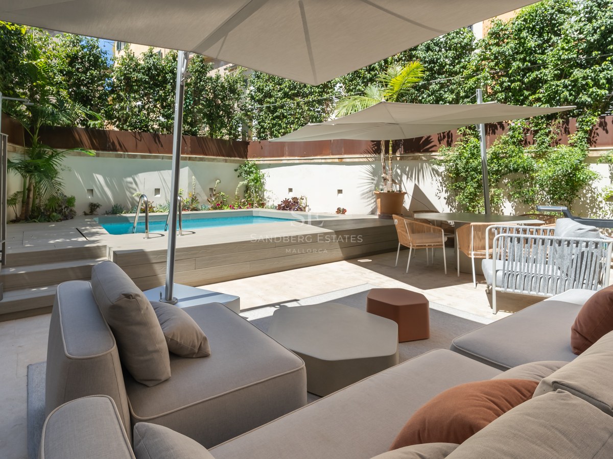Sun-drenched terrace featuring a private pool, modern grey sofas with terracotta pillows, and large white umbrellas.