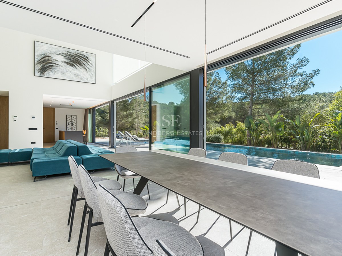 Utomhusvy av modern villa med infinitypool, solstolar, gräsmatta och panoramautsikt. Minimalistisk arkitektur med stora fönsterpartier.