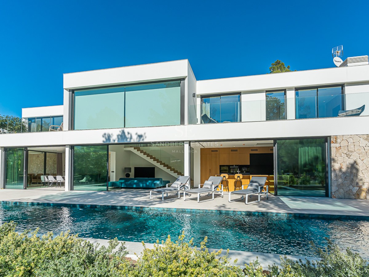 Exteriör vy av ett modernt hus med pool, lummig trädgård och stora fönster. Elegant design och högkvalitativa ytskikt.