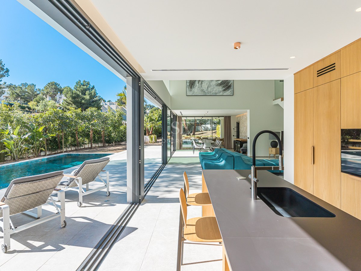 Vy av modern villa med infinitypool, solstolar och anlagd trädgård. Minimalistisk design med stora fönster och rikligt med naturligt ljus.