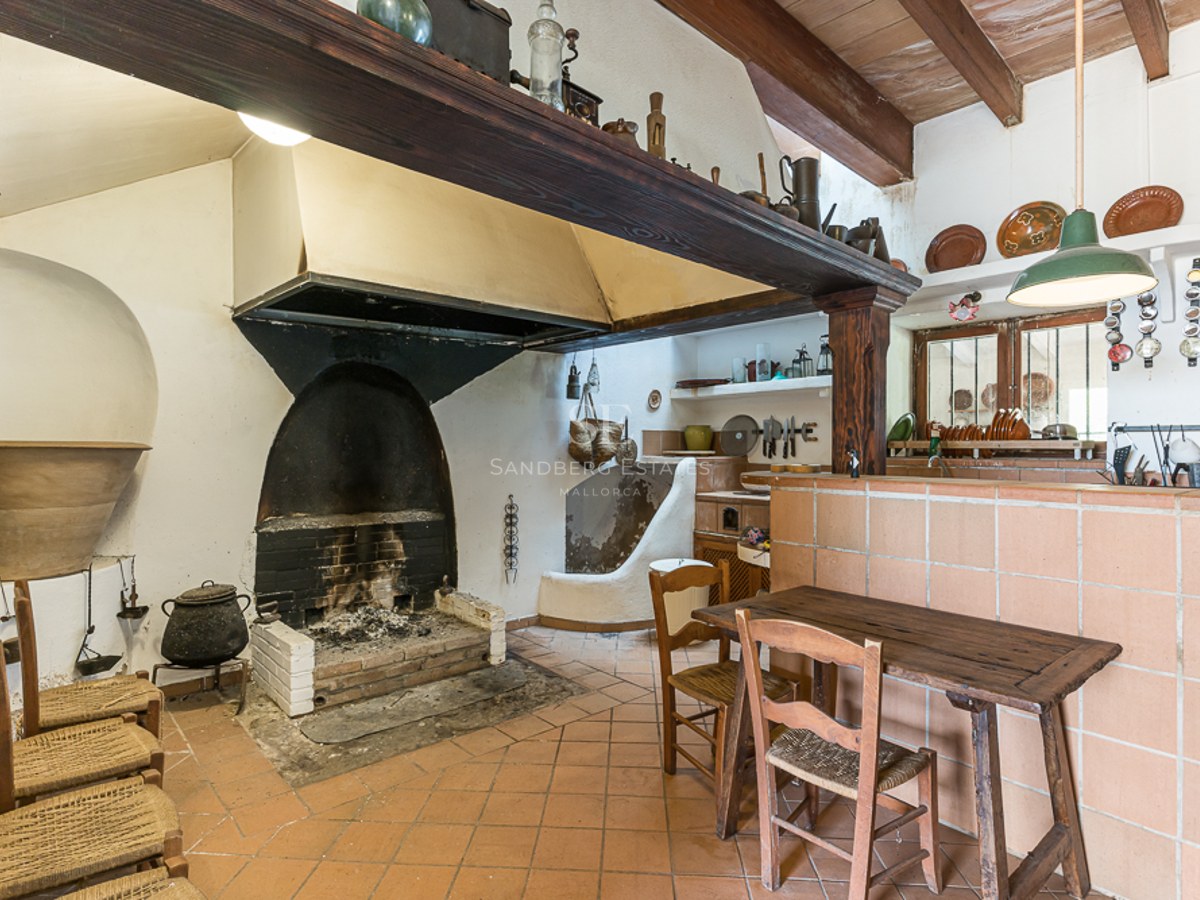 Rustic kitchen with a large open hearth fireplace, terracotta tile floor, and traditional wooden furniture.