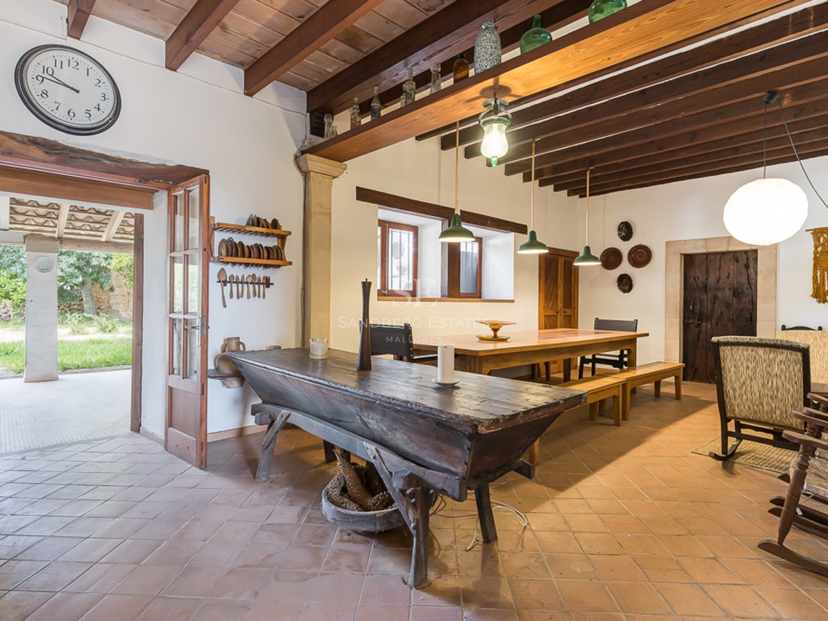 Rustic dining room with terracotta floors, exposed wooden beams, a long table, and antique furniture.
