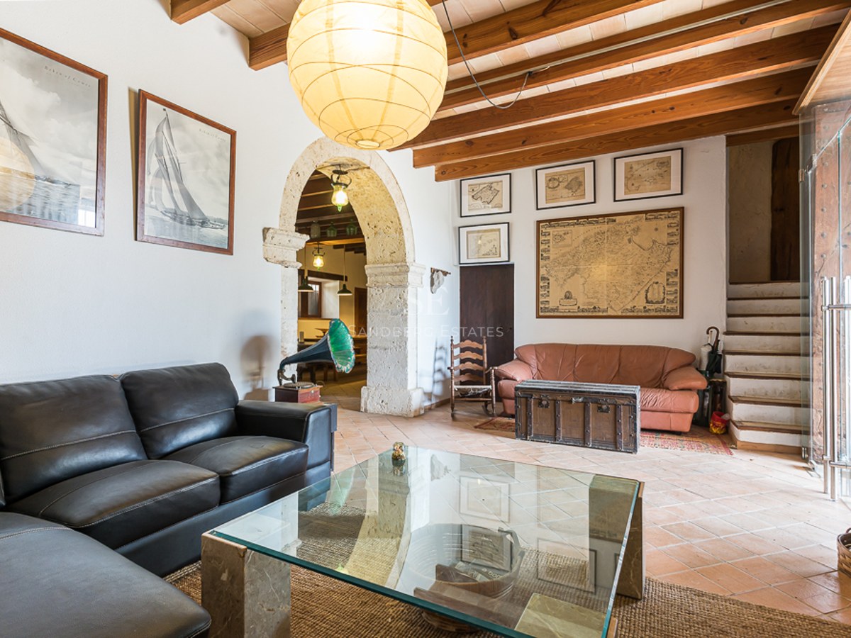 Living room with leather sofas, glass coffee table, stone archway, wooden beams, and terracotta tiles.