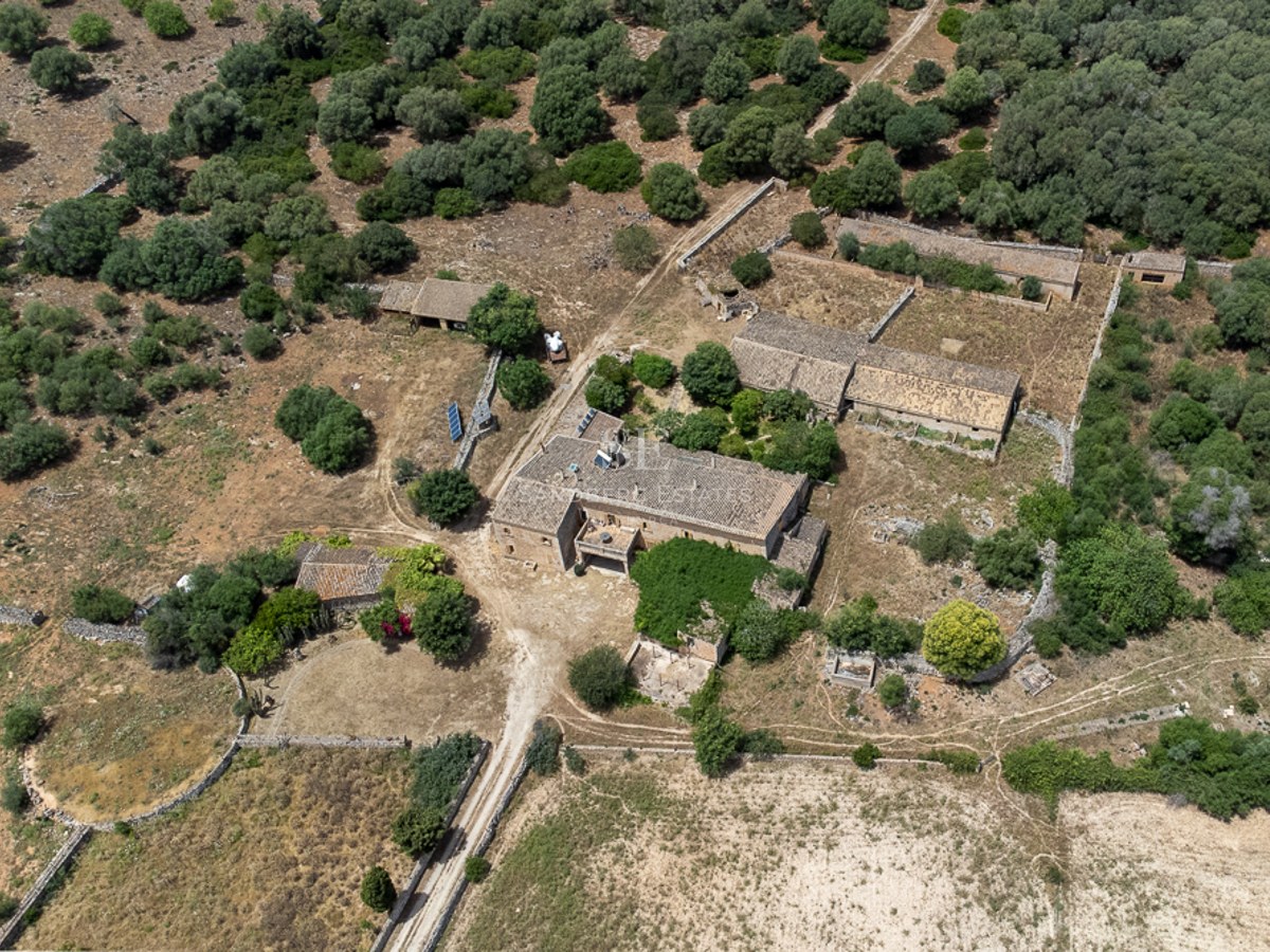 Aerial view of a large rural compound with traditional stone buildings surrounded by Mediterranean vegetation.